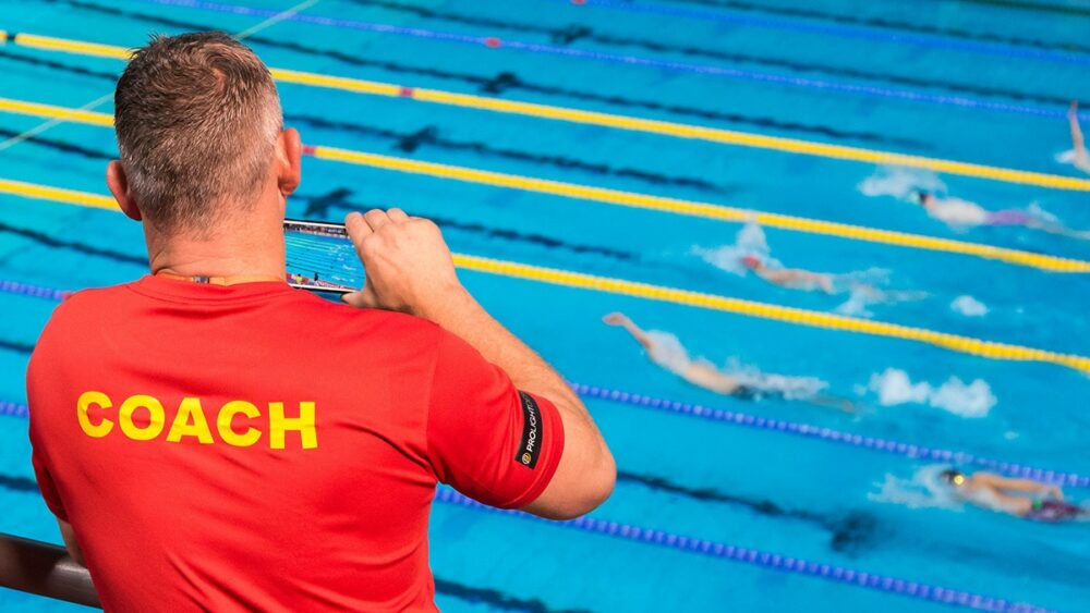 An elite swim coach reviewing an AI coaching philosophy training plan with a swimmer at the poolside.